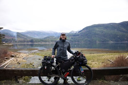 Man enjoys a scenic view with loaded bicycle by the tranquil lake.