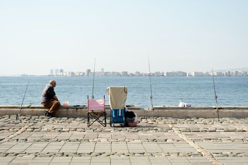 Free A serene scene of a man fishing on the İzmir promenade with the cityscape in the background. Stock Photo