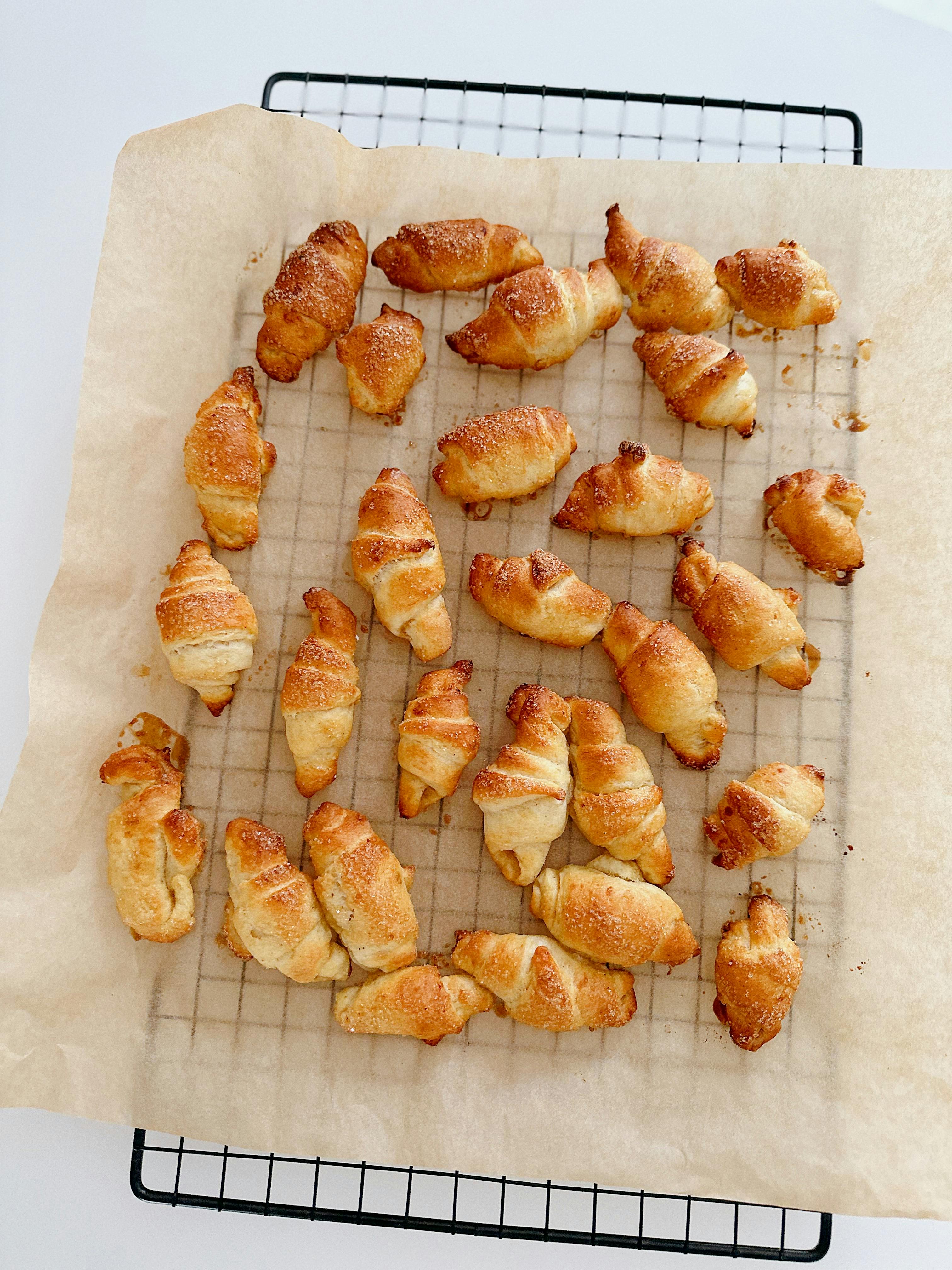 A batch of homemade golden-brown croissants on a cooling rack arranged on parchment paper.