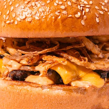 Mouthwatering close-up of a cheeseburger with crispy onions and sesame seed bun.