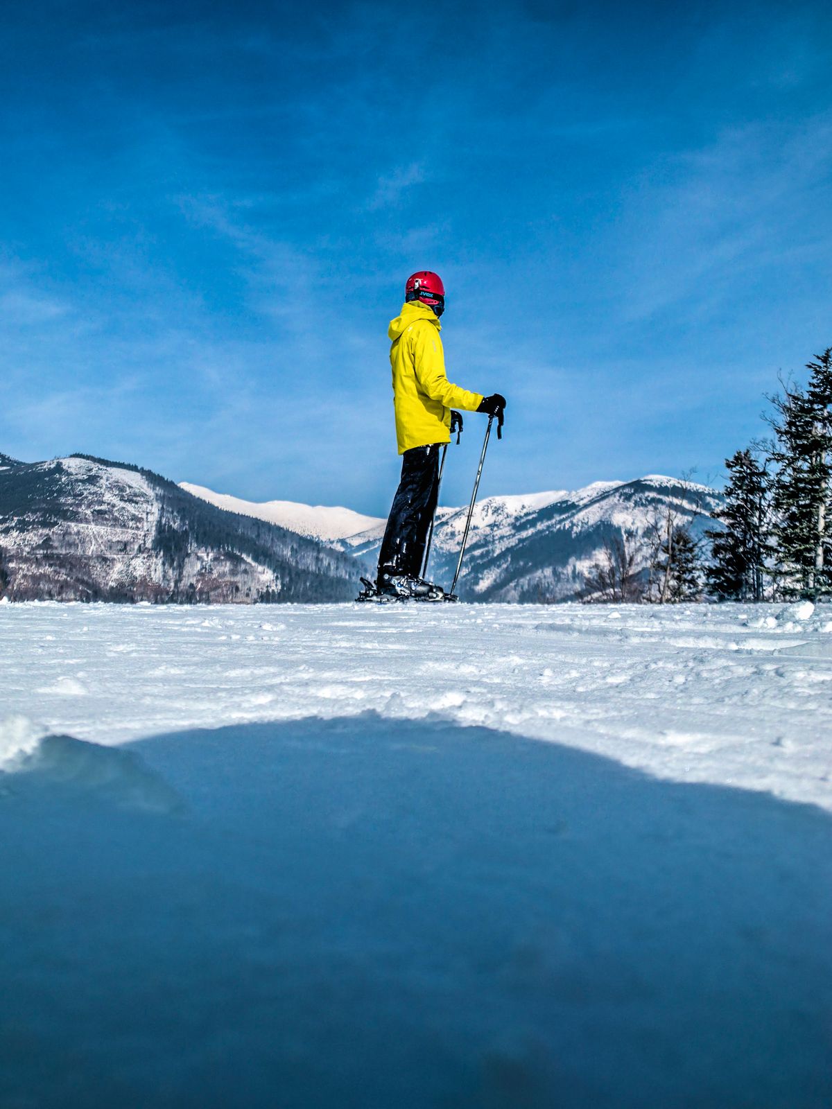 A skier in a yellow jacket standing on a snowy mountain ridge
