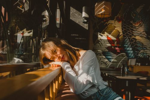 Free Warm sunlight bathes a serene woman leaning in an artistic café with vivid wall art. Stock Photo