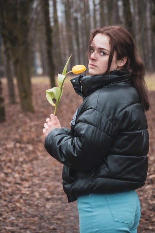 Young Woman Standing in a Forest in Autumn and Holding a Tulip 