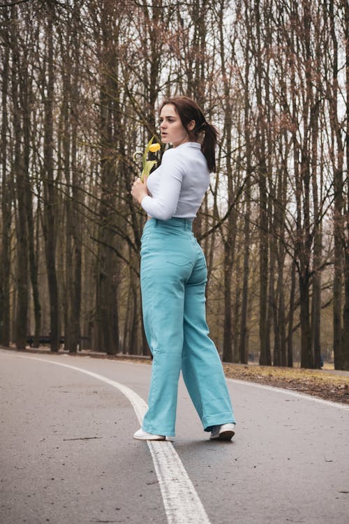 Young Woman Standing on a Street near Autumnal Trees and Holding a Tulip 