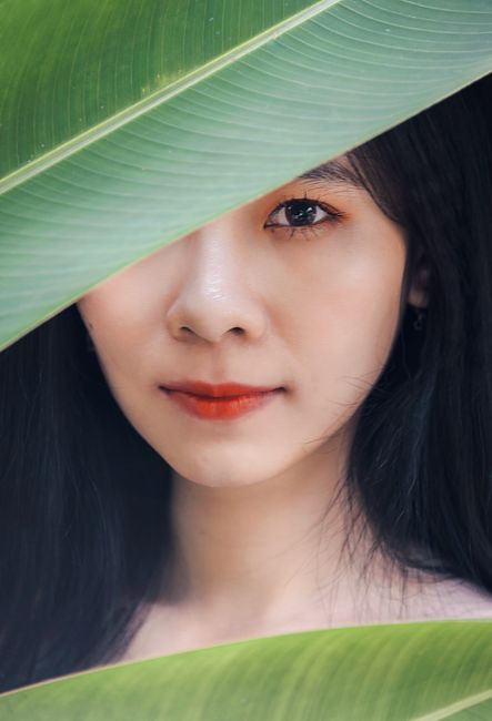 Captivating portrait of a woman partially hidden behind vibrant green leaves.