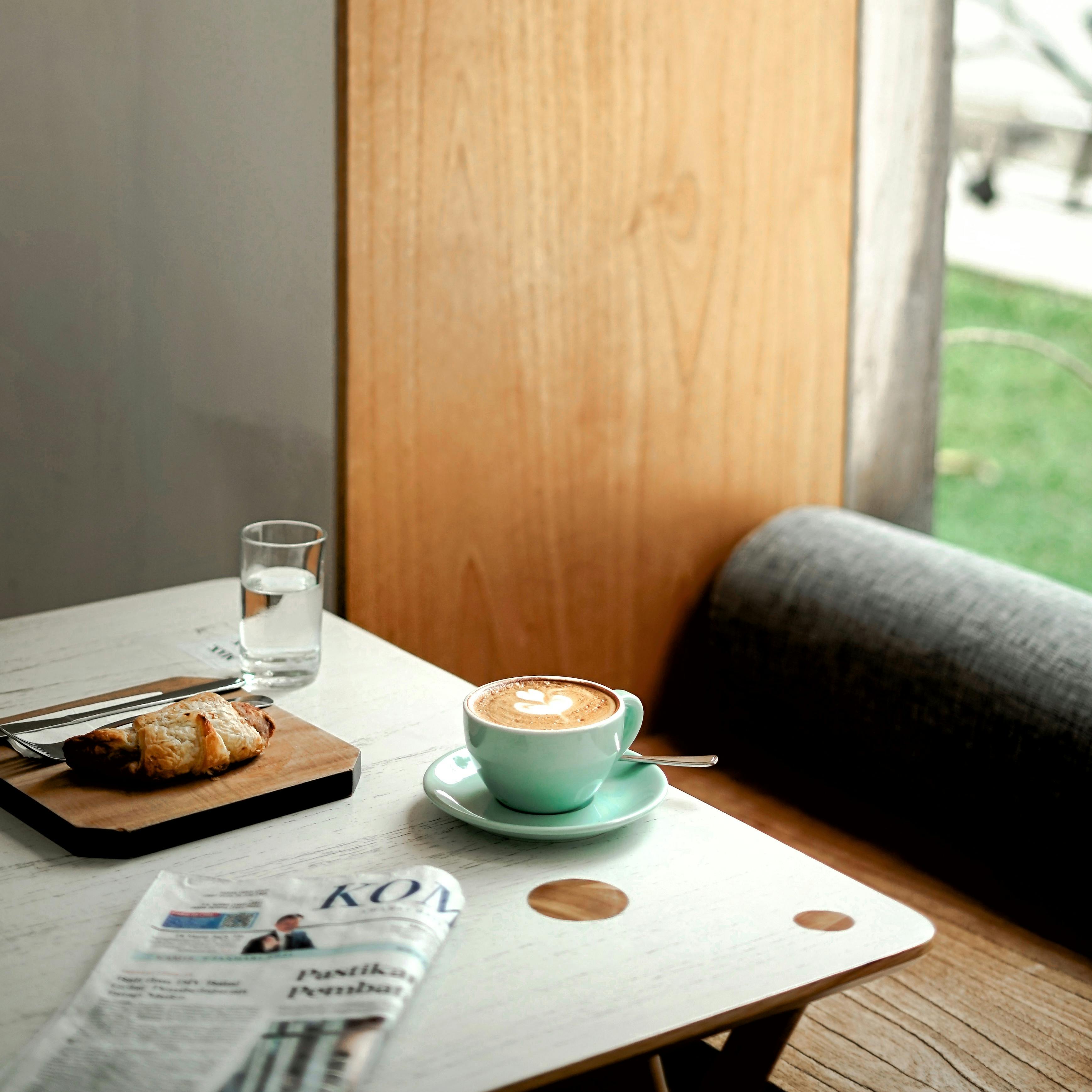 A cozy morning scene with cappuccino, croissant, and newspaper in a Semarang cafe.