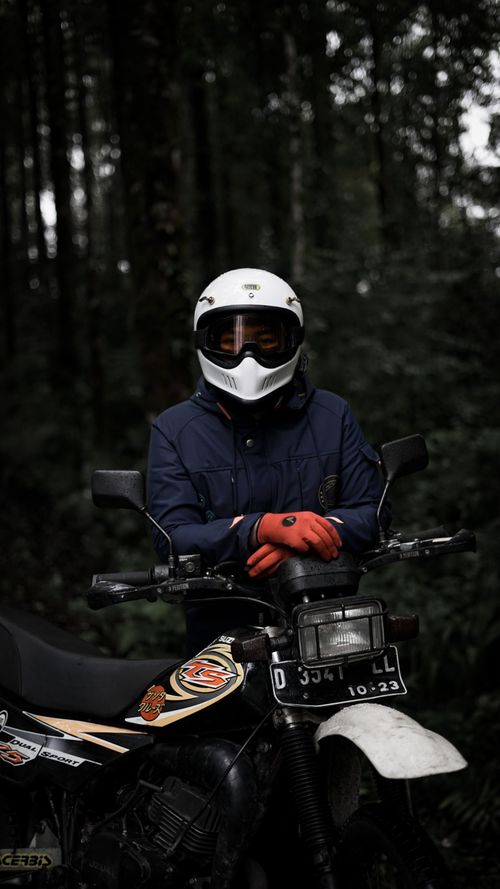 Free A biker with a helmet poses in a dense forest, resting on a motorcycle. Stock Photo