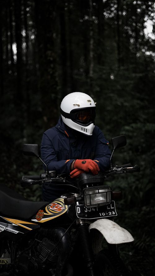 Free Motorcyclist wearing safety gear pauses on a motorcycle amidst dense forest surroundings. Stock Photo