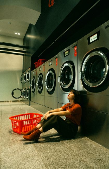 A young woman sitting with eyes closed beside washing machines in a laundromat.