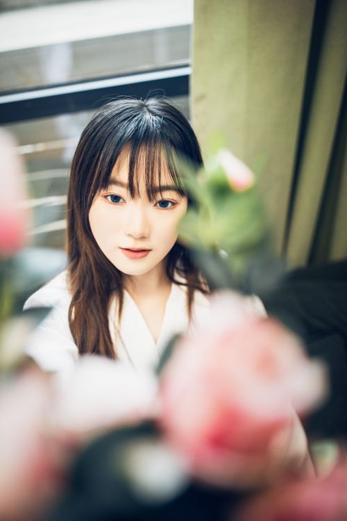 Free Elegant portrait of a young woman indoors with soft focus on flowers. Stock Photo