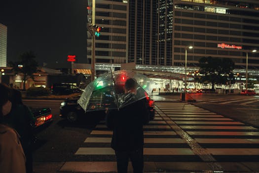 Person with umbrella crossing a city street at night, captured in a rainy downtown setting.