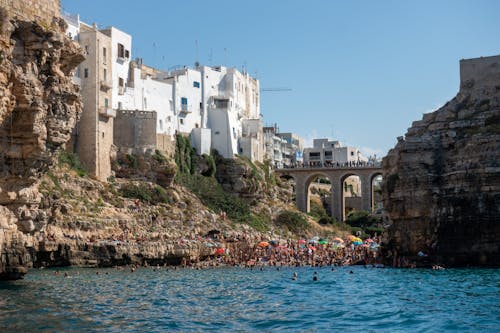 People Swimming in Sea near Coastal Town on Rocks