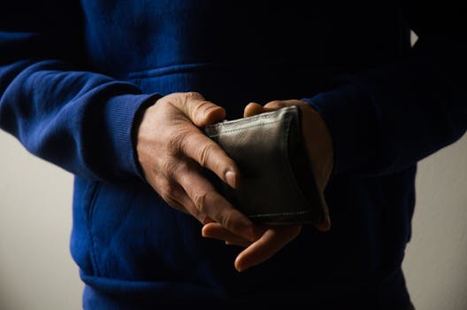 A man in a blue hoodie holding a leather wallet, symbolizing finances or personal belongings.