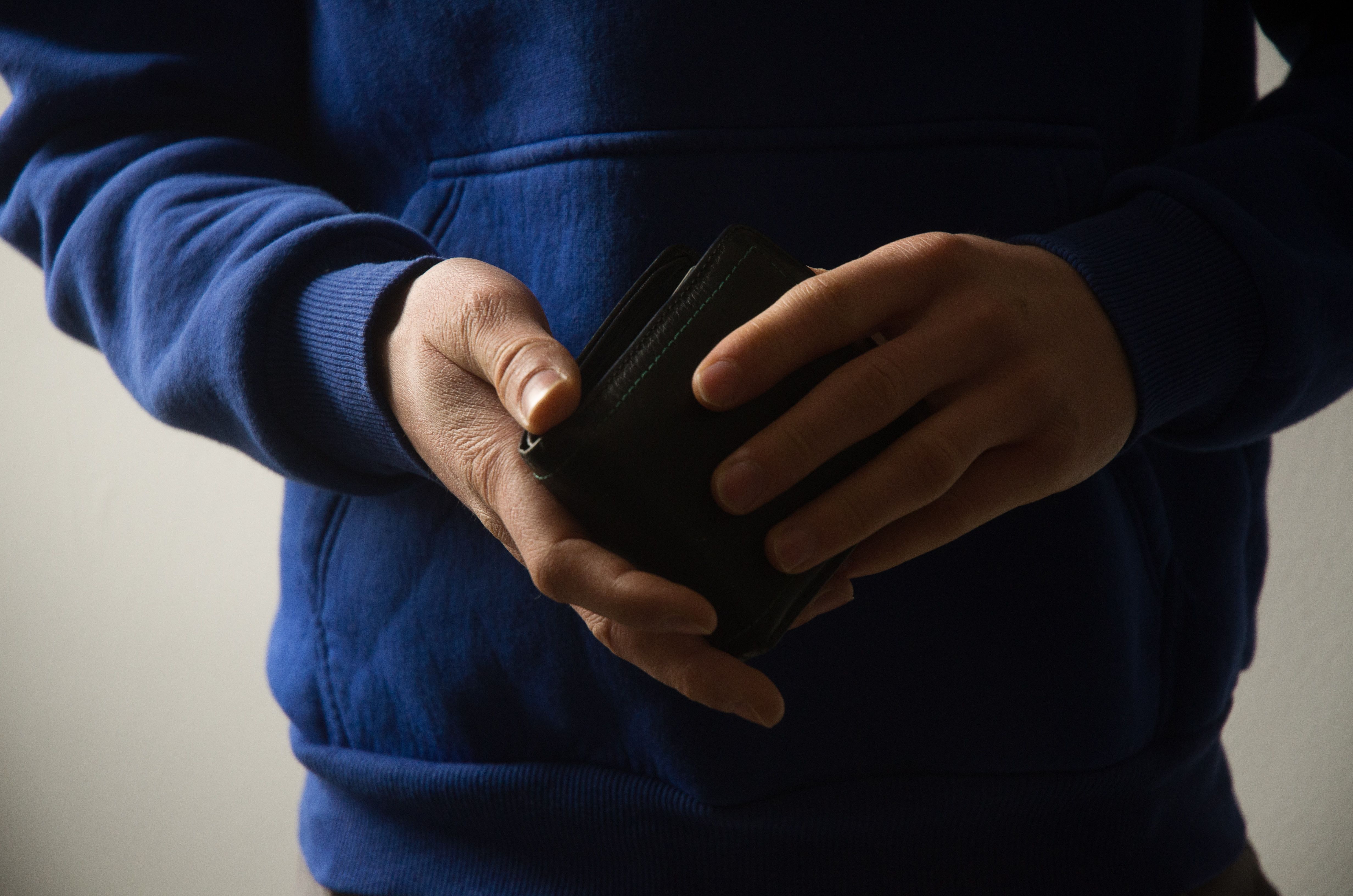 Close-up of a man holding a wallet, showcasing casual menswear style in a blue hoodie.
