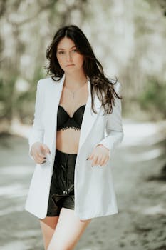 Confident brunette posing in a chic outfit with a black bra and white jacket. Outdoor setting.