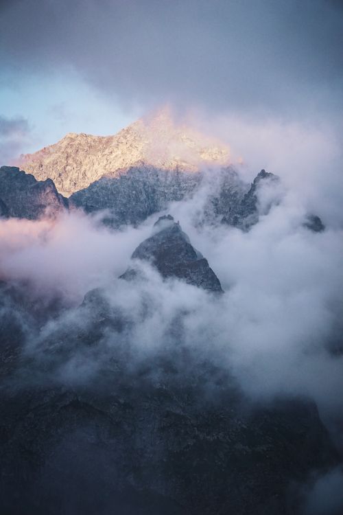 Free Stunning view of mountain peaks enveloped in misty clouds at sunrise, offering a serene and majestic landscape. Stock Photo