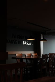 A dark, modern restaurant interior with wooden chairs and tables under pendant lighting.