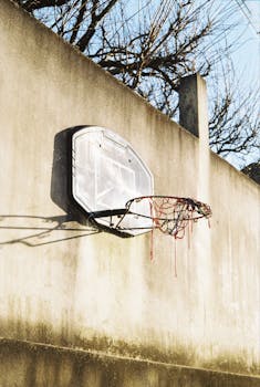 A sunlit, weathered basketball hoop on a wall in Barcelos, capturing urban sports culture.