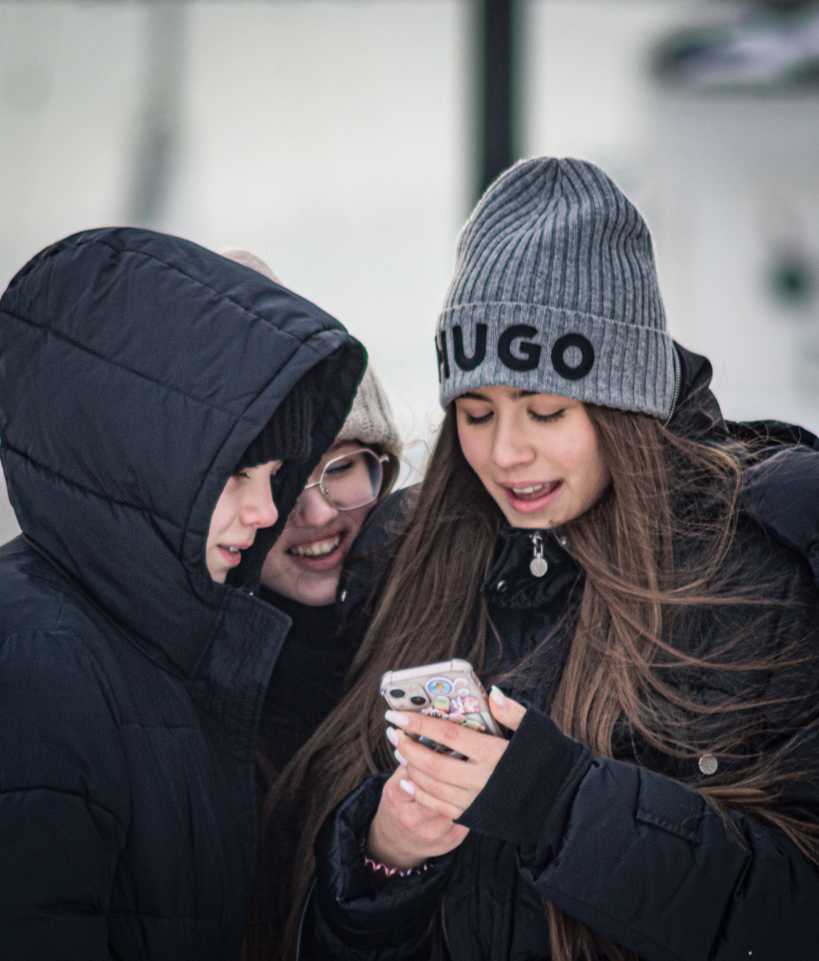 Three teenagers having fun outdoors in winter, sharing moments on a smartphone.