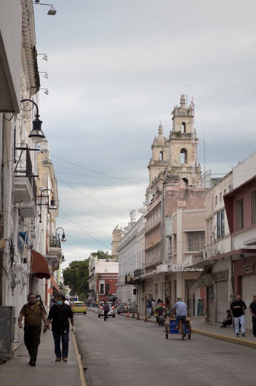 Pedestrians Walking on a Sidewalk in City between Buildings and a Church in the Background 