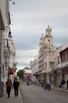 Bustling street scene with colonial architecture in Mérida, Yucatan, Mexico under cloudy skies.