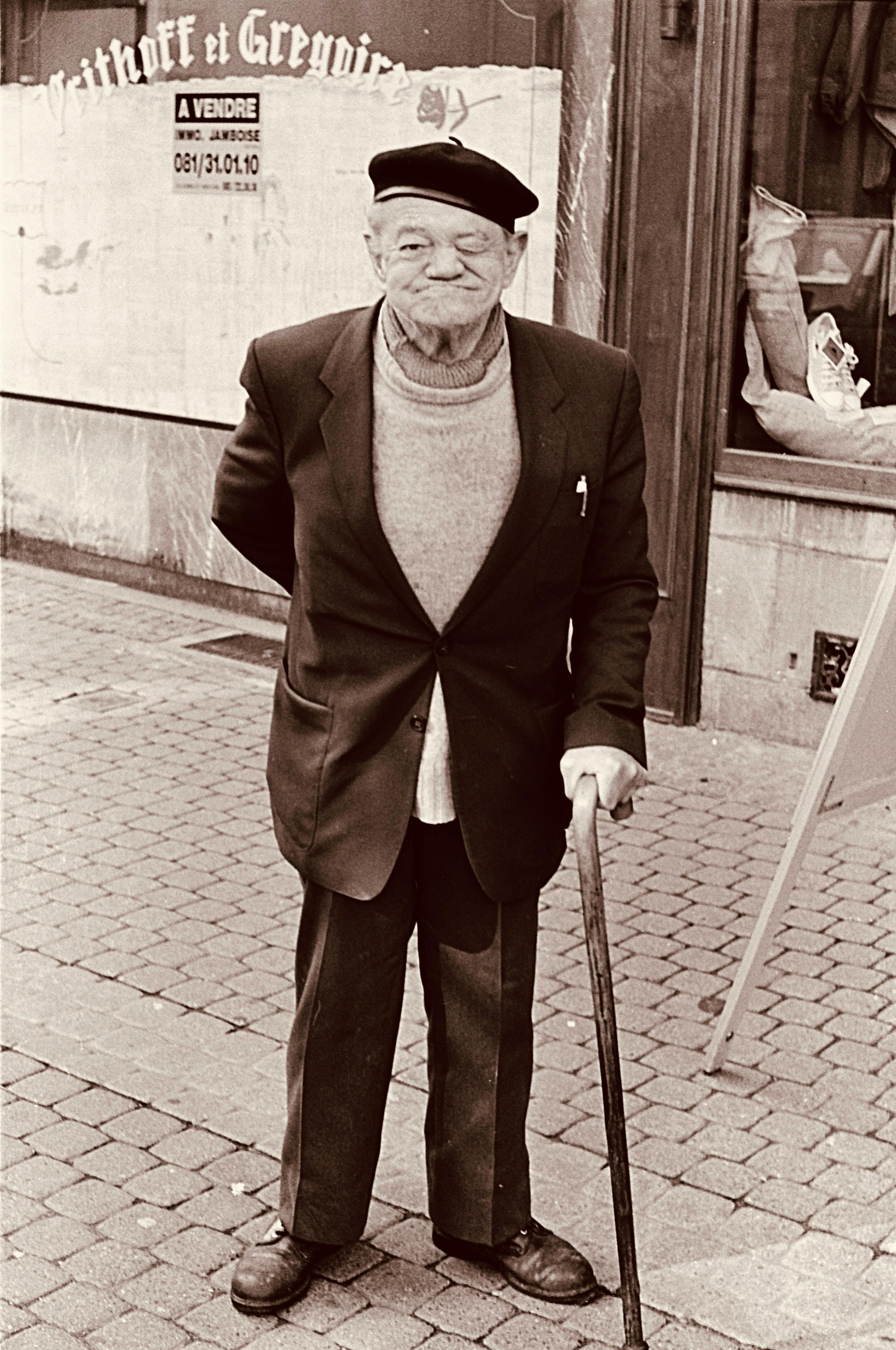 Sepia-toned portrait of an elderly man with a cane on a cobblestone street in Namur, Belgium.
