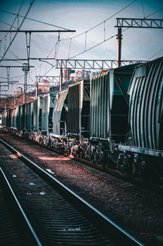 Long freight train on railway tracks in an urban area with overhead cables.