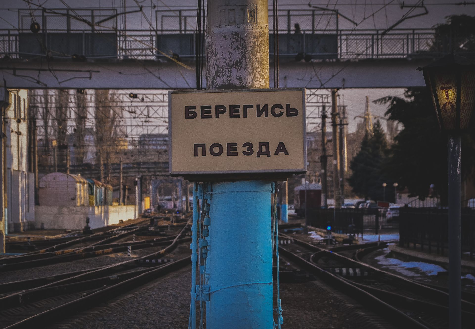Close-up of a railway warning sign with Russian text against an urban infrastructure backdrop.