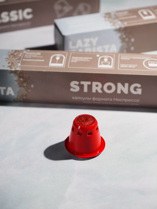 Free Close-up of a red coffee capsule with packaging in soft sunlit setting. Stock Photo