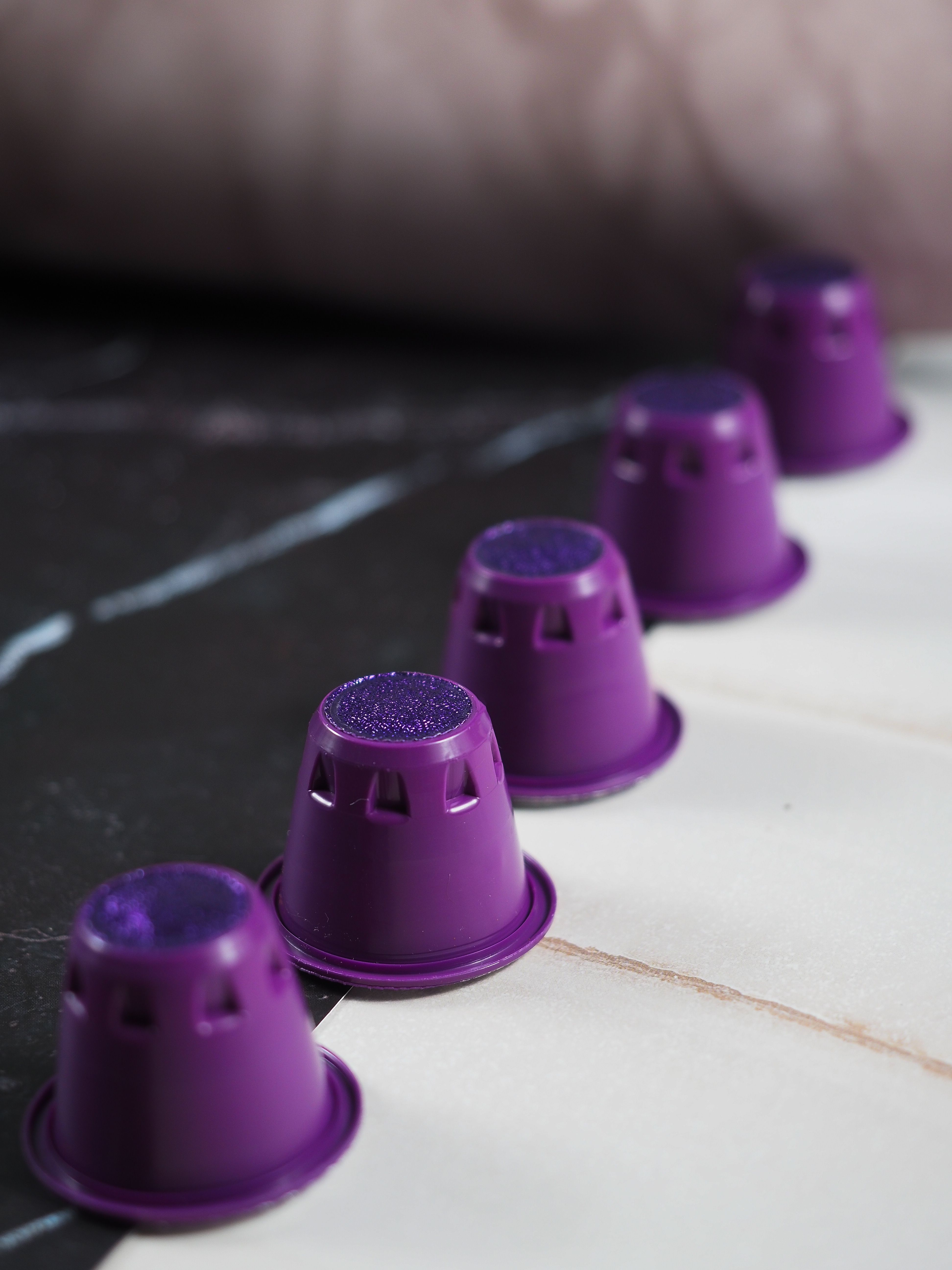 Close-up of purple coffee capsules neatly lined up on a marble surface, showcasing vibrant color and modern design.