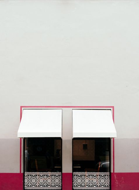 A minimalist facade with two white awnings on a pink and white wall.