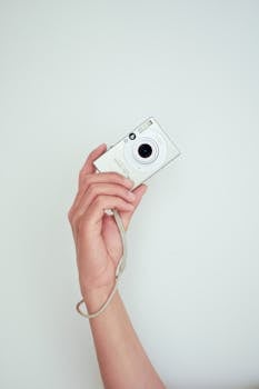 A hand holds a compact digital camera against a clean white background, ideal for photography themes.