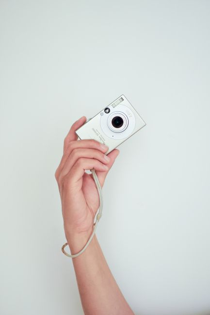 A hand holds a compact digital camera against a clean white background, ideal for photography themes.