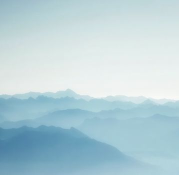 A serene and ethereal mountain range enveloped in mist under a tranquil sky, perfect for atmospheric and calming themes.