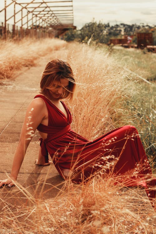 Female Model Wearing a Red Dress Sitting at the Edge of a Paved Footpath