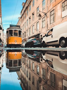 Yellow tram and city buildings mirrored in a puddle on a Lisbon street, capturing Lisbon's charm.