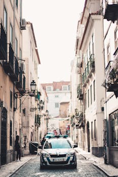 A bustling alleyway in Madrid featuring a police car and classic architecture under bright daylight.