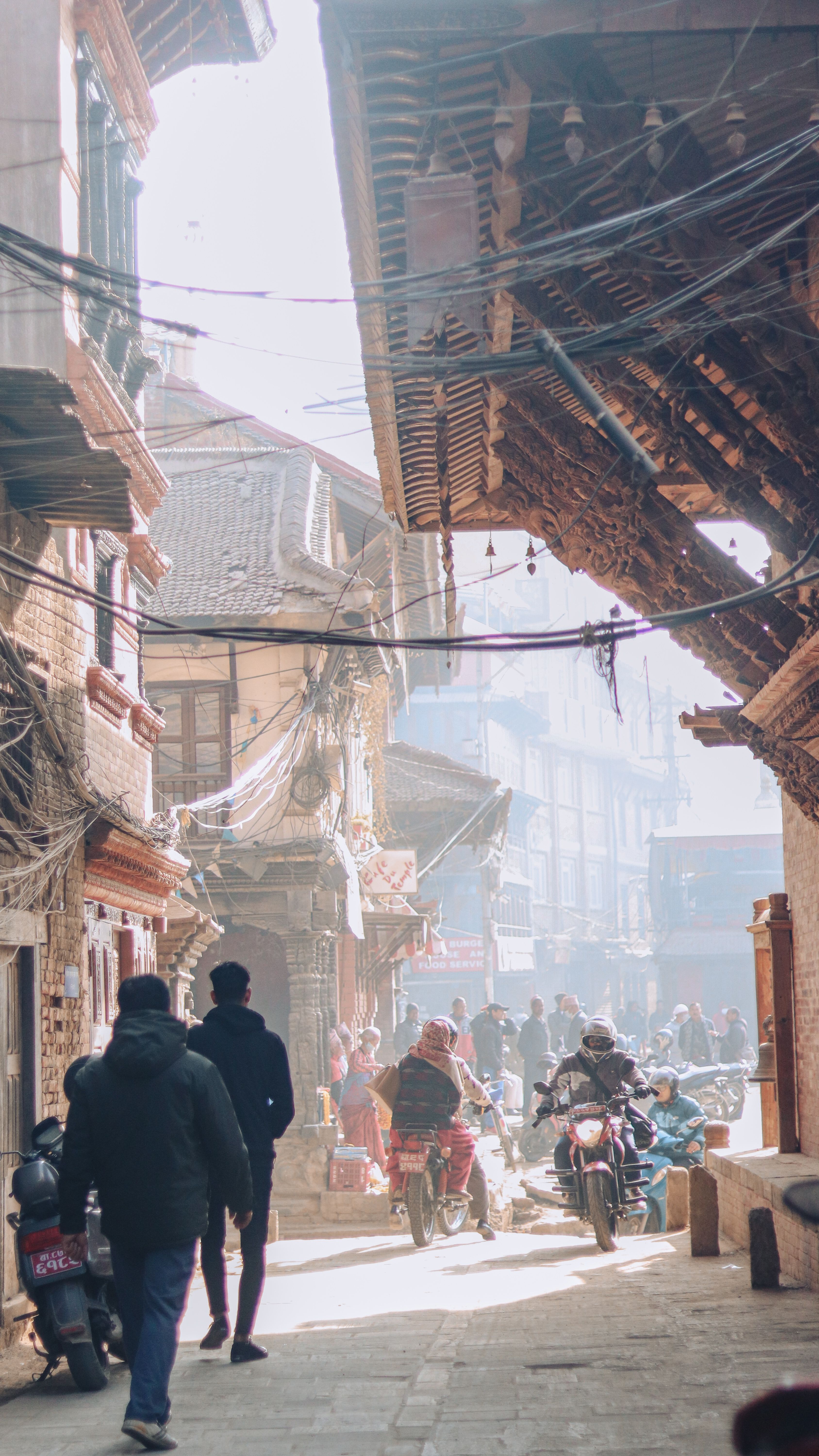 Lively street market in Bhaktapur, Nepal with people, motorcycles, and traditional architecture.