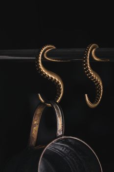 Intricate brass hooks hold a rustic pot against a black background, creating an artistic minimalist scene.