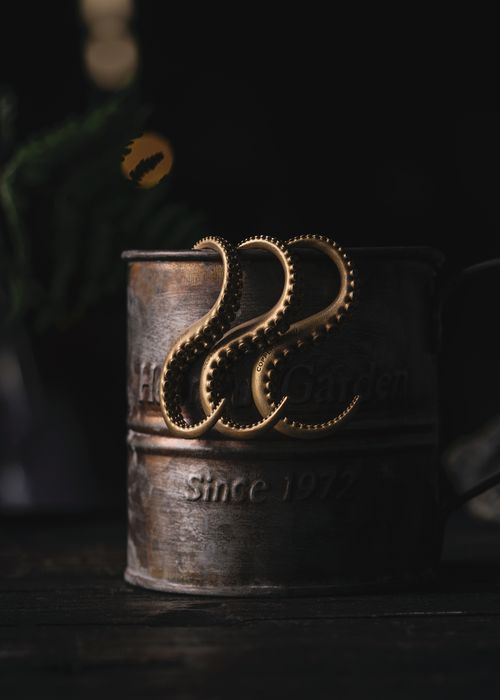 Free A rustic metal cup adorned with elegant golden octopus-shaped earrings, creating a moody still life. Stock Photo