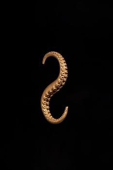 Intricate bronze octopus tentacle hook against a dark black background in a vertical shot.