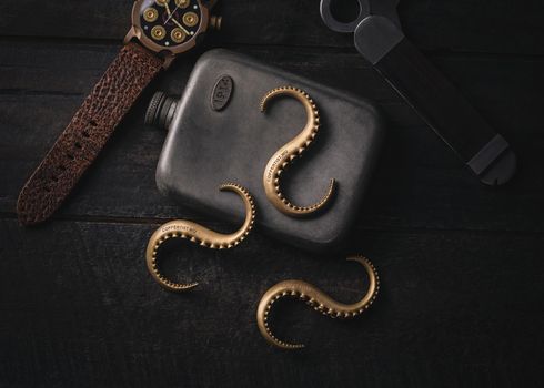 A dark vintage-themed still life with a flask, watch, and octopus tentacle hooks.