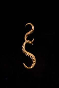 A close-up of an ornate brass octopus tentacle piece set against a black background, capturing intricate details.