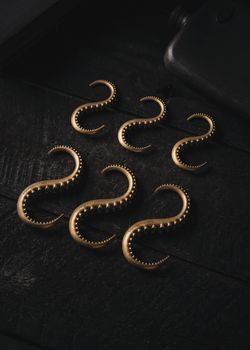 Vintage brass octopus tentacle hooks arranged on a dark wooden surface displayed in a still life setting.
