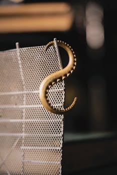 A stylish golden octopus-shaped hook elegantly hangs on a metal mesh fence.