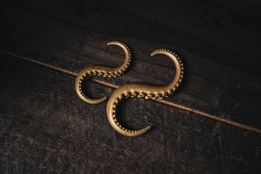 Close-up of ornate vintage brass octopus tentacle hooks on a rustic wooden background.