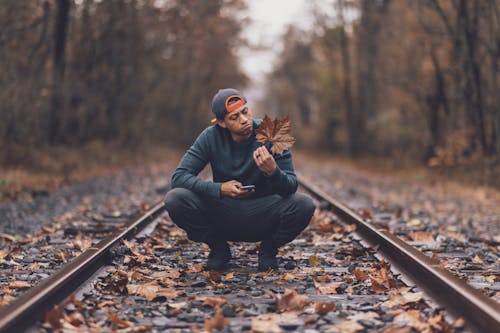 Man Holding Maple Leaf In The Middle Of Train Tracks During Day