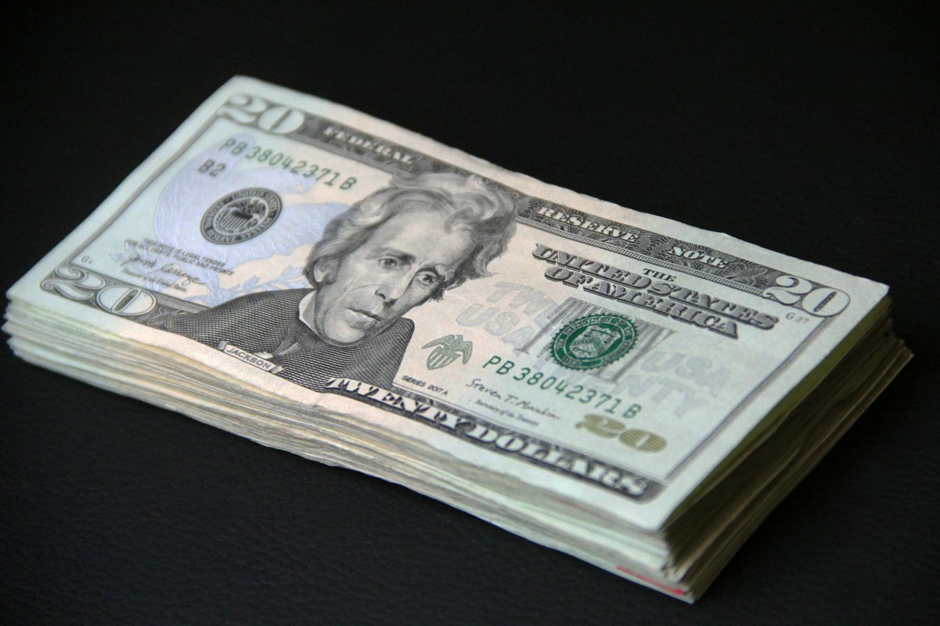 A close-up of a stack of American 20 dollar bills against a black background, symbolizing wealth.