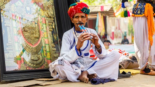 Man in Traditional Clothing and a Turban Sitting on the Street and Playing a Flute 