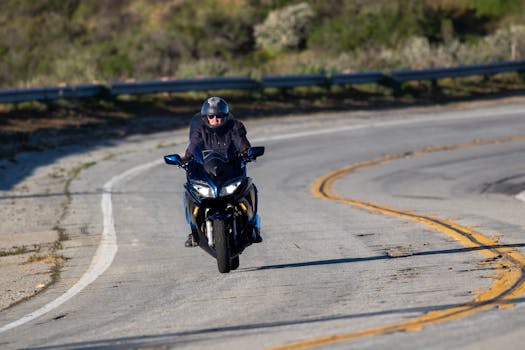 A man in a helmet rides a motorcycle on a winding road in a sunlit, rural setting.